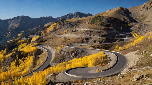 Winding paved mountain highway climbing above treeline with golden aspen stands on the lower slopes in Colorado
